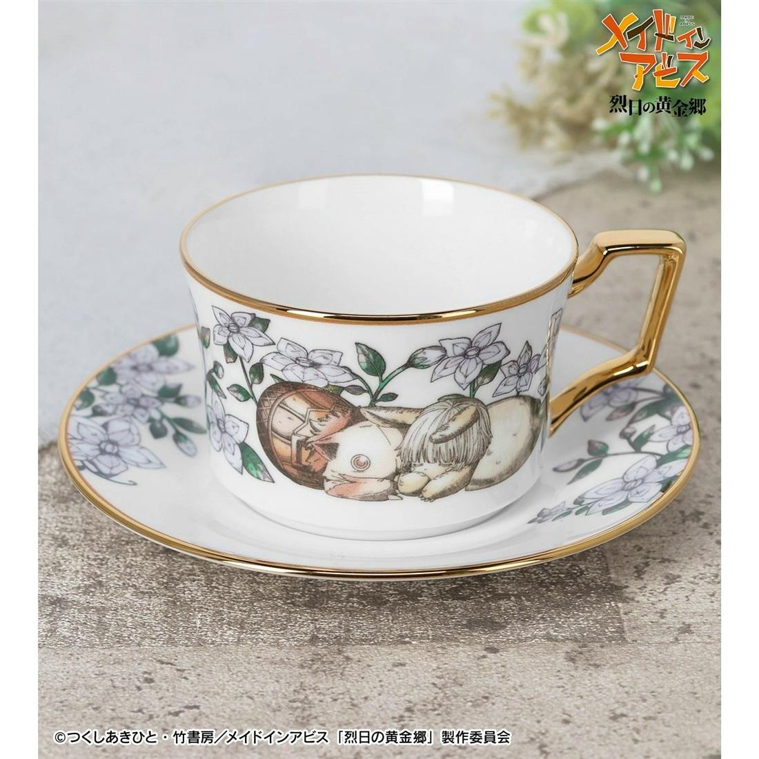White ceramic tea cup and matching saucer decorated with Nanachi and Mitty illustrations and gold trim.