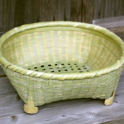 Woven bamboo tea-bowl draining basket with short feet, shown empty on a wooden surface.