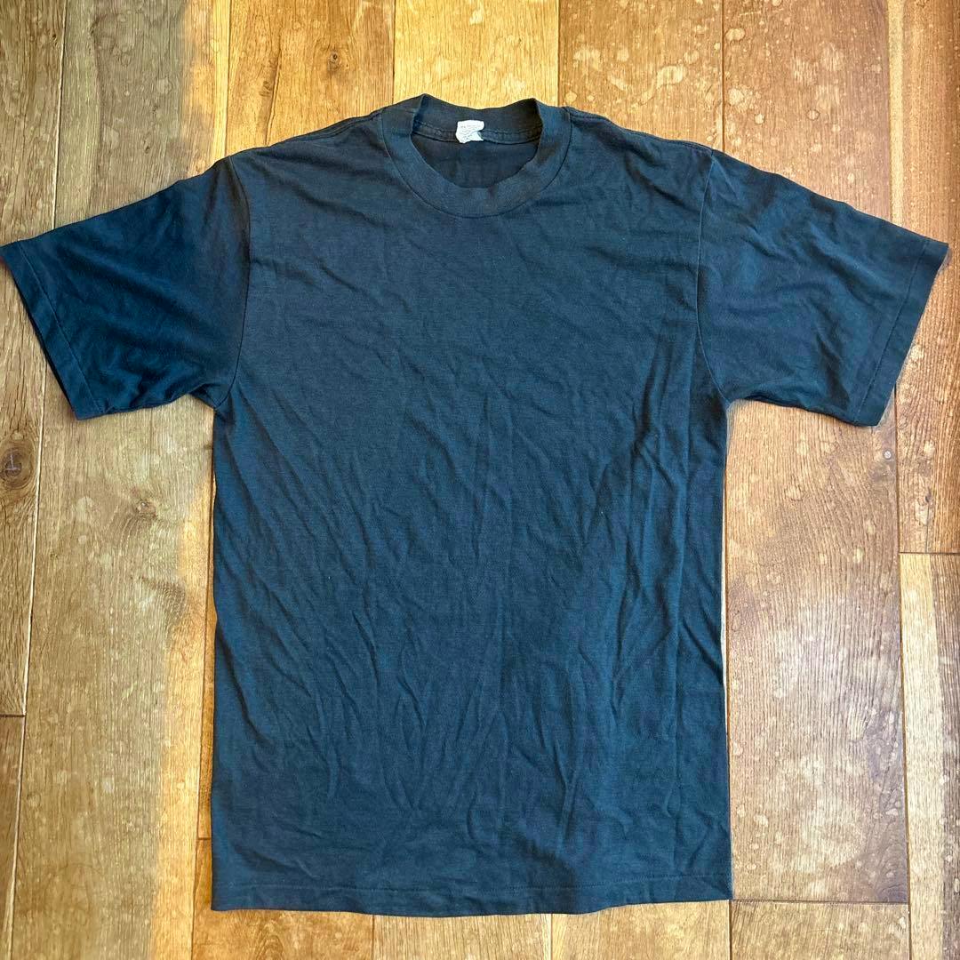 Black plain men's cotton T-shirt laid flat on a wooden floor showing the front.