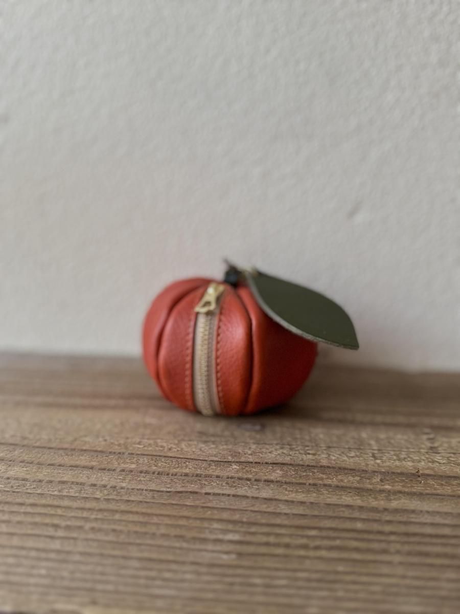 Italian leather mini pouch shaped like a mandarin orange in dark orange with a green leaf, photographed on a wooden surface.