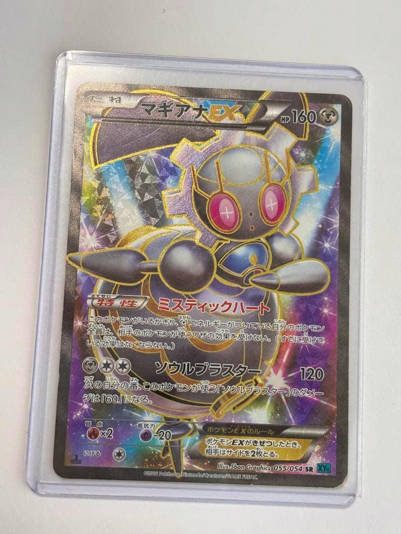 Photo of the マギアナEX SR Pokémon trading card front in a protective sleeve, showing the full card artwork and Japanese text.