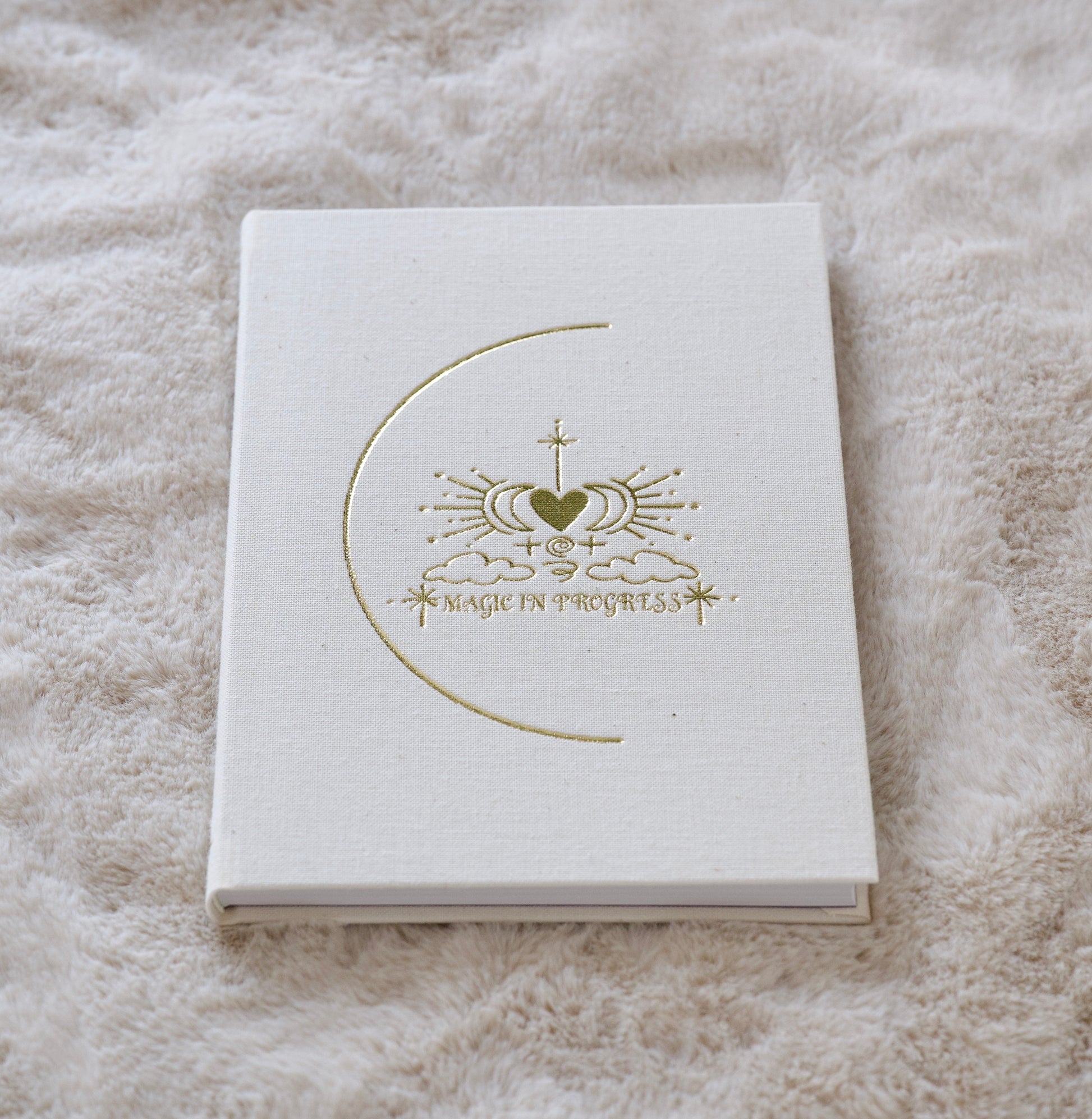 White notebook with a gold crescent and emblem stamped on the cover lying on a soft textured surface.