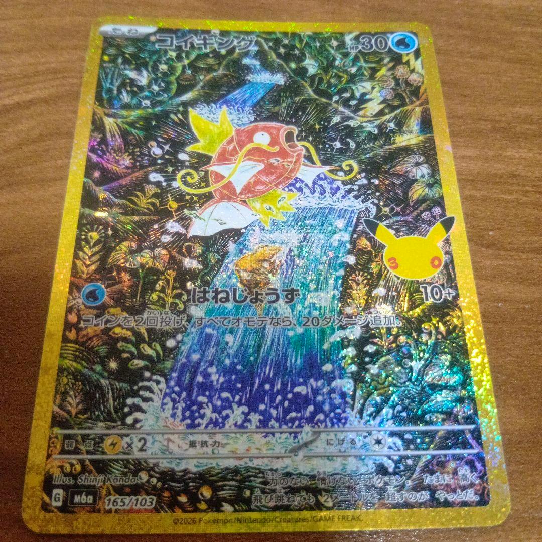 Photograph of the holographic コイキングar trading card (165/103) with a gold border and 30th Pikachu icon, placed on a wooden surface.