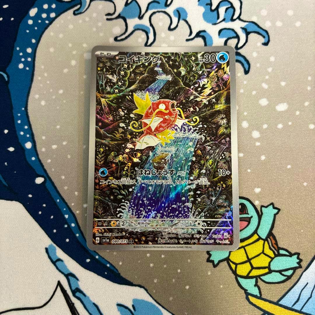 Front of the Magikarp (コイキング) Japanese trading card showing the holographic artwork placed on a patterned playmat.