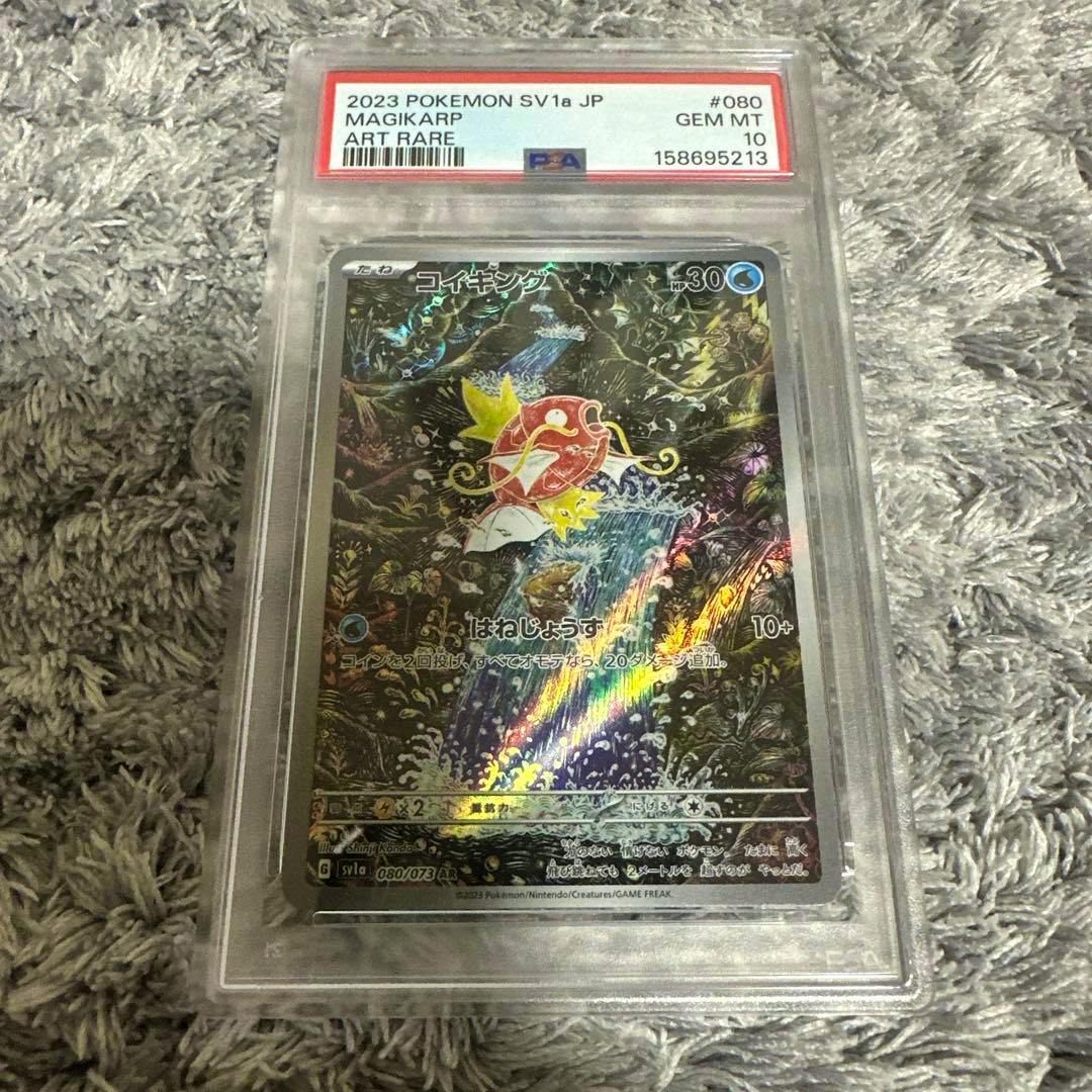 Front of the コイキング (Magikarp) AR SV1a holographic trading card shown inside a PSA slab on a carpeted surface.