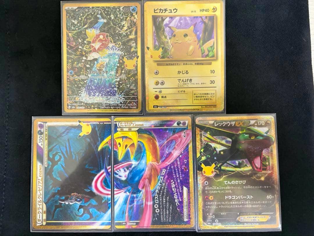 Photograph of multiple Pokémon trading cards including コイキング, ピカチュウ, ダークライ&クレセリア LEGEND, and レックウザEX laid out on a black background.