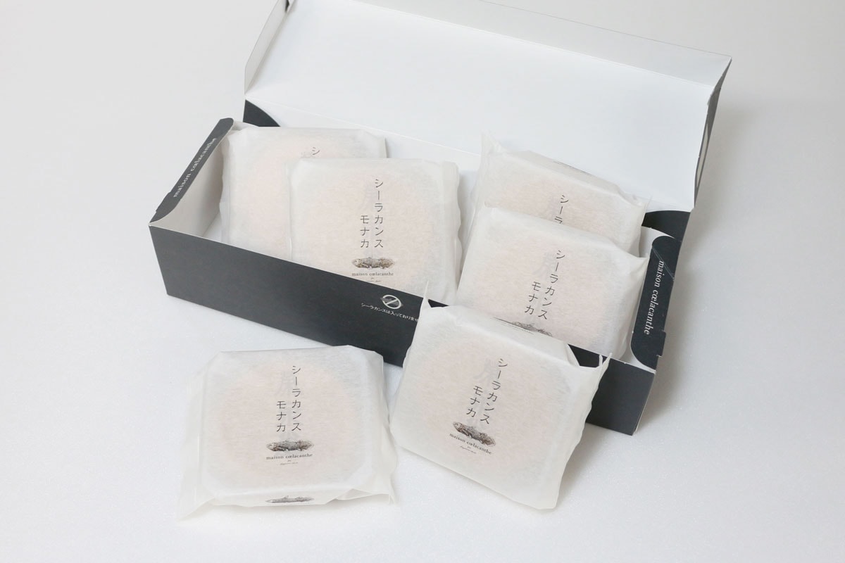 Opened simple box of six individually wrapped シーラカンス モナカ cakes with two packages placed outside the box.