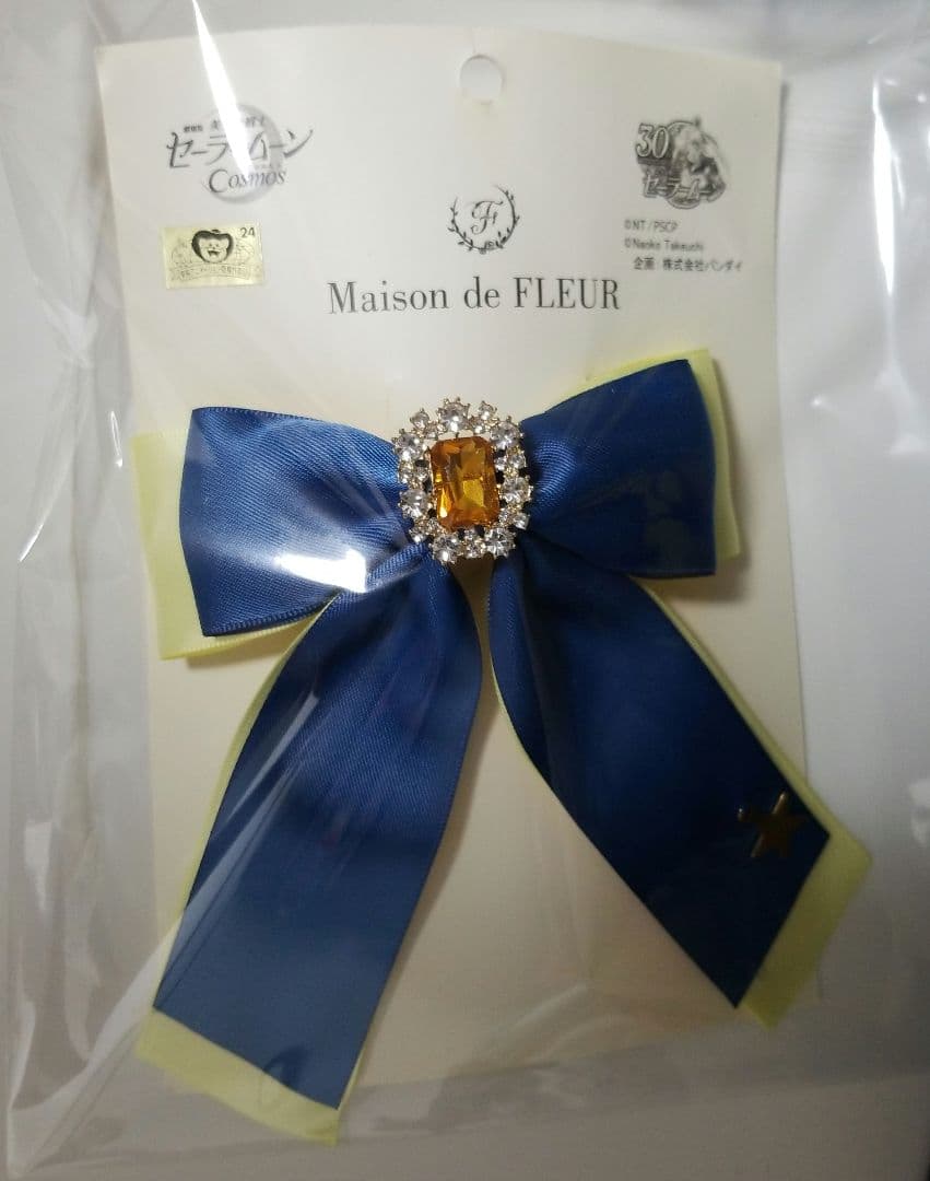Maison de FLEUR ribbon barrette: a blue and pale yellow bow with a central amber jewel on a branded backing card inside plastic packaging.