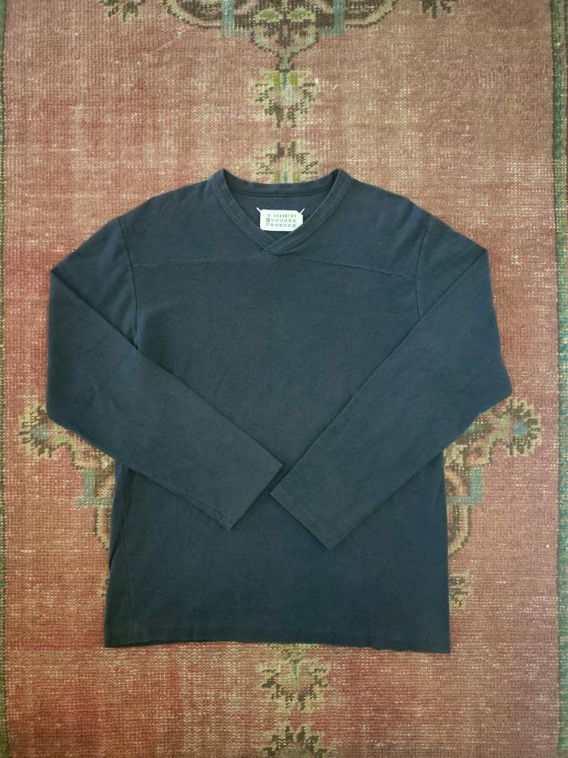 Front view of a dark long-sleeve men's cotton T-shirt laid flat on a patterned rug with the label visible at the neckline.