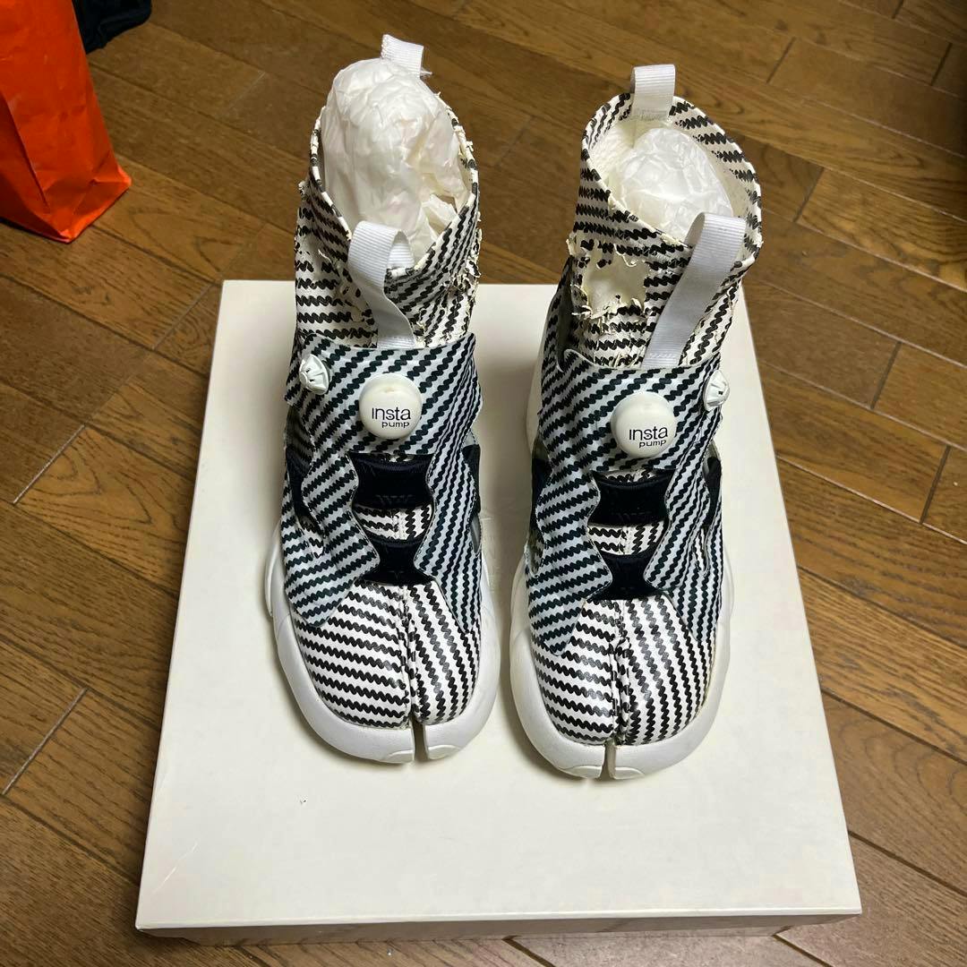Pair of Maison Margiela x Reebok split-toe (tabi) sneakers in a black-and-white zigzag pattern displayed on a white shoebox.