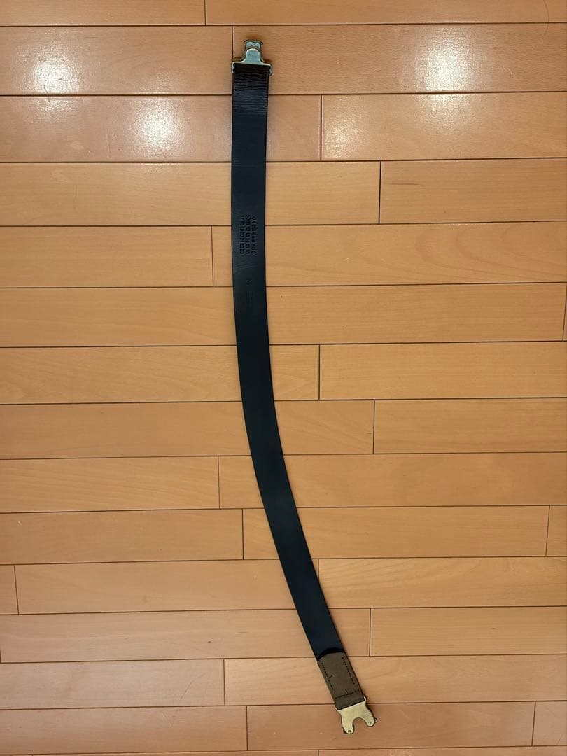 Full-length synthetic leather belt with a brass cobra buckle laid flat on a wooden floor.