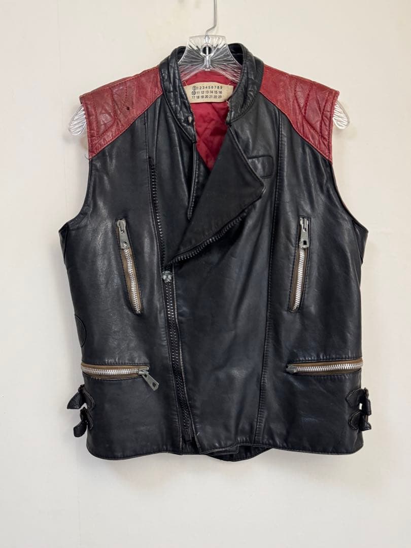 Front view of the Martin Margiela 2003 artisan biker vest in black cow leather with red shoulder panels hanging on a hanger.