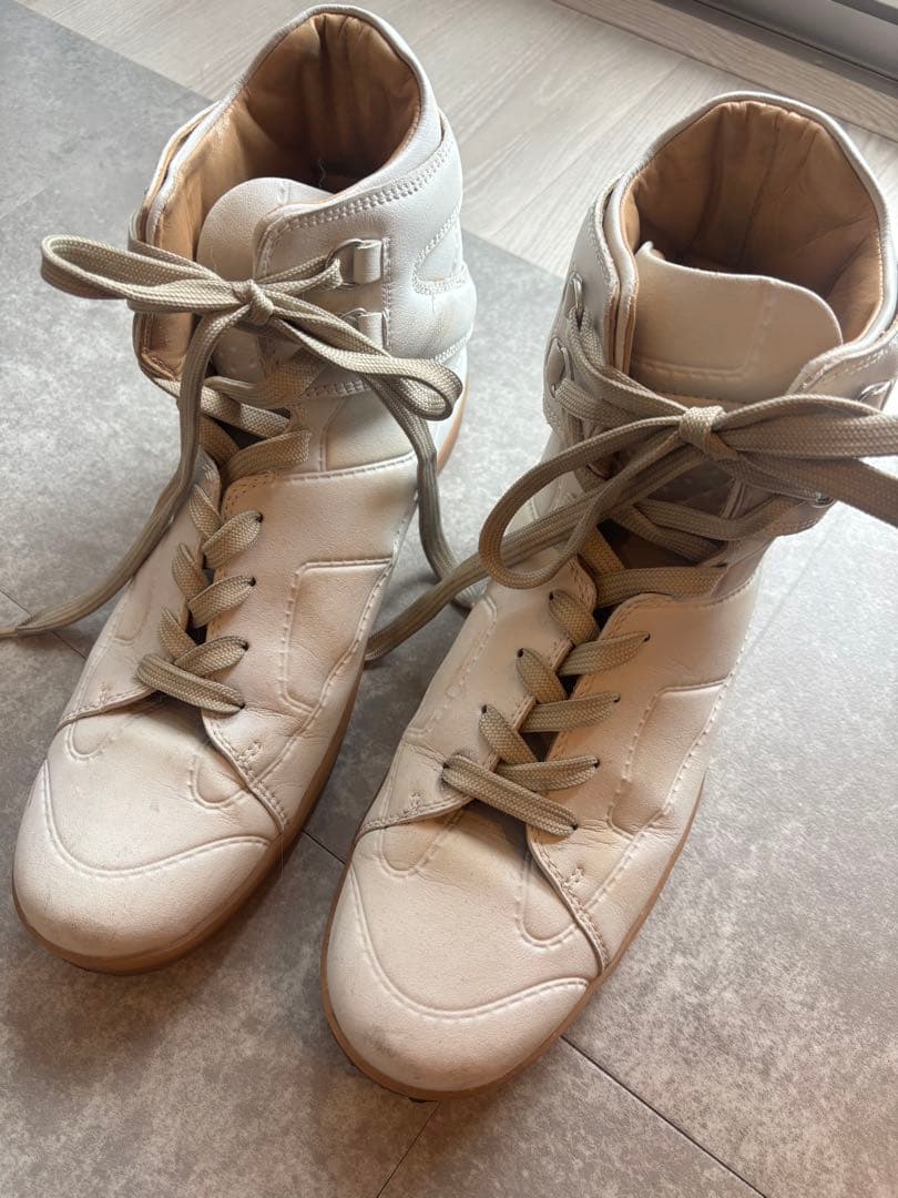 Pair of white high-top sneakers (マルジェラ x H&M コラボ) placed on a floor, shown from an angled top view.