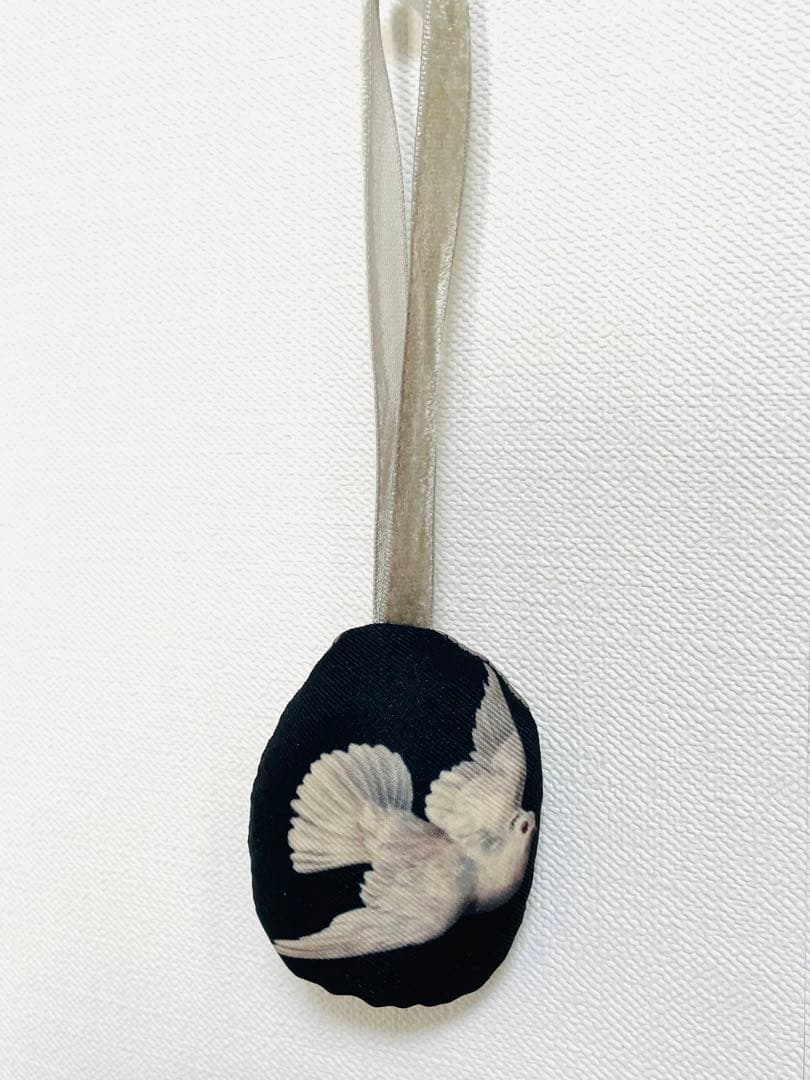 Fabric oval ornament with a printed white dove on a dark background hanging from a pale ribbon.