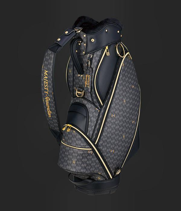 Black Majesty×Resurrection Oriola caddy bag with gold hardware and shoulder strap against a dark background.