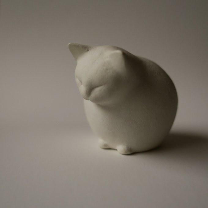 A white ceramic figure of a sleeping cat on a plain neutral background.