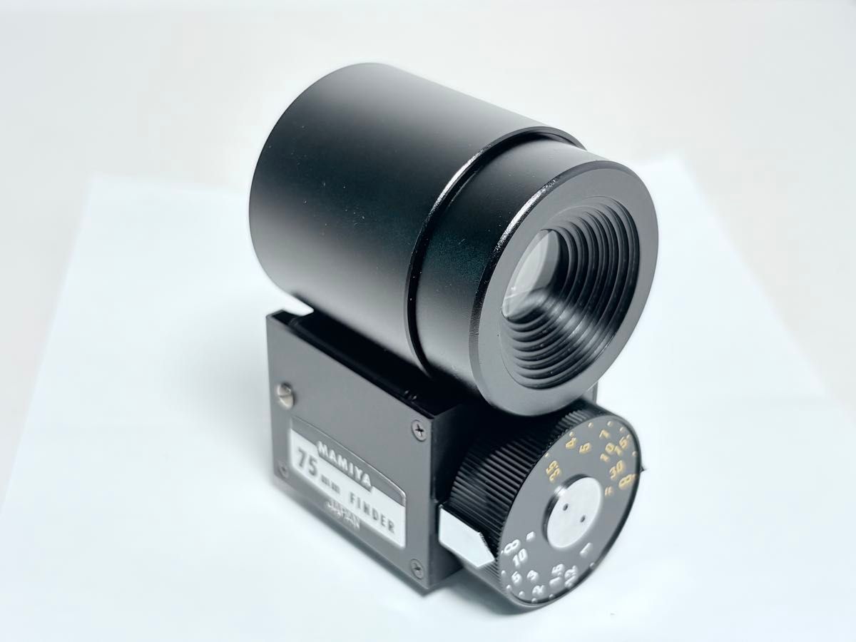 Black Mamiya 75mm viewfinder on a white background, shown at an angle with its eyepiece, side label, and focus dial visible.
