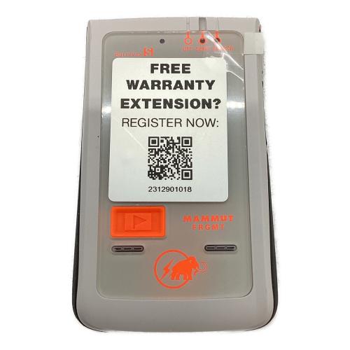 Front view of the white MAMMUT Barryvox S FRGMT Edition transceiver with an orange button and a warranty registration sticker on the front.