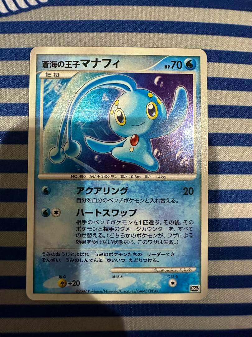 Front view of the trading card 蒼海の王子マナフィ (10th movie anniversary premium sheet) showing the holographic artwork on a striped fabric background.