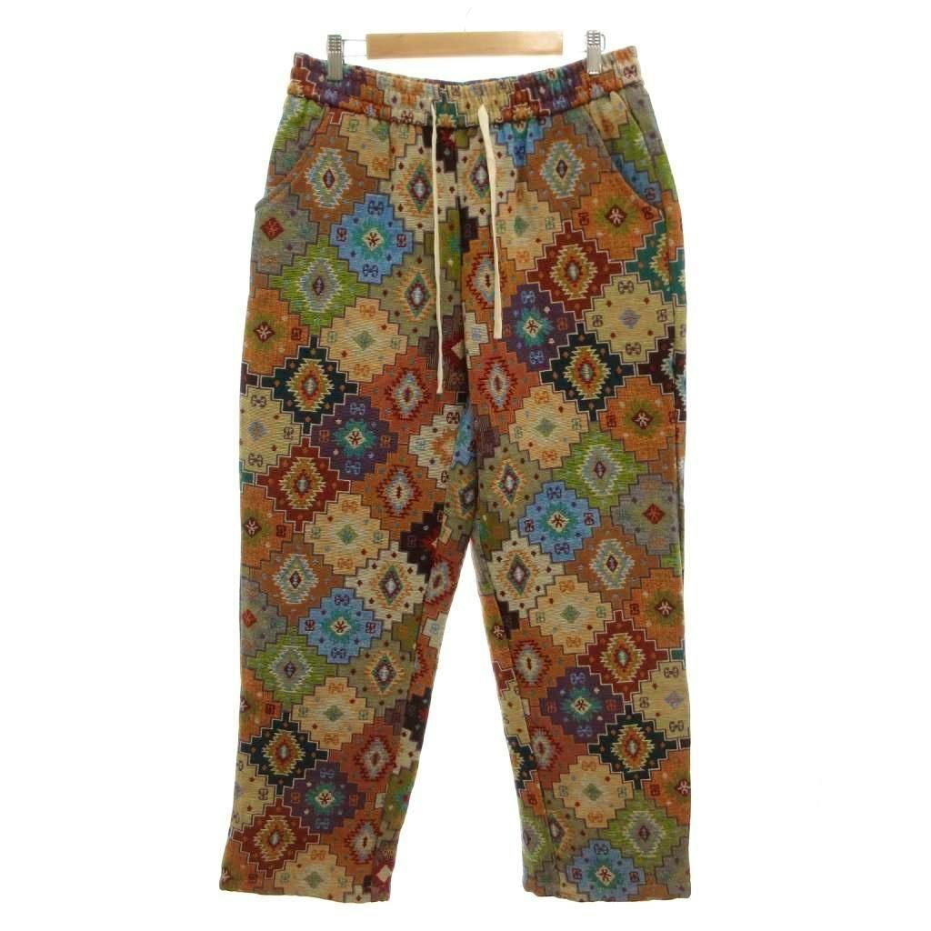 Front view of men's drawstring pants with an orange multicolor geometric pattern hanging on a wooden hanger.