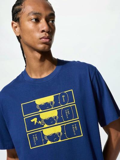 Close-up of a model wearing a blue cotton T-shirt from the Manga UT マッシュル-MASHLE- collection with a yellow comic-strip style print on the chest.