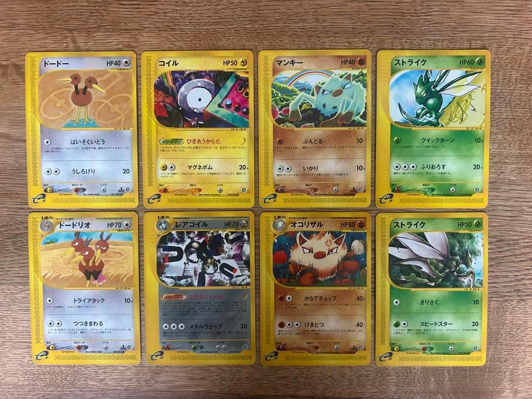 Eight Japanese Pokémon trading cards including マンキー and オコリザル laid out on a wooden surface.