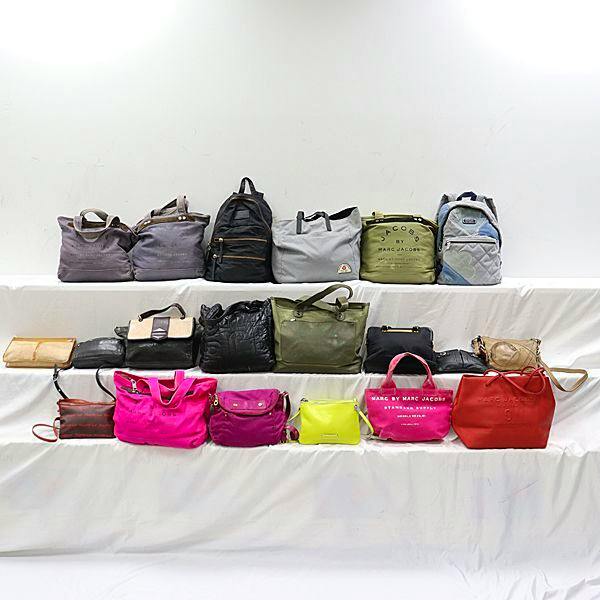 Multiple Marc by Marc Jacobs canvas bags in various colors arranged on three white tiers against a white background.