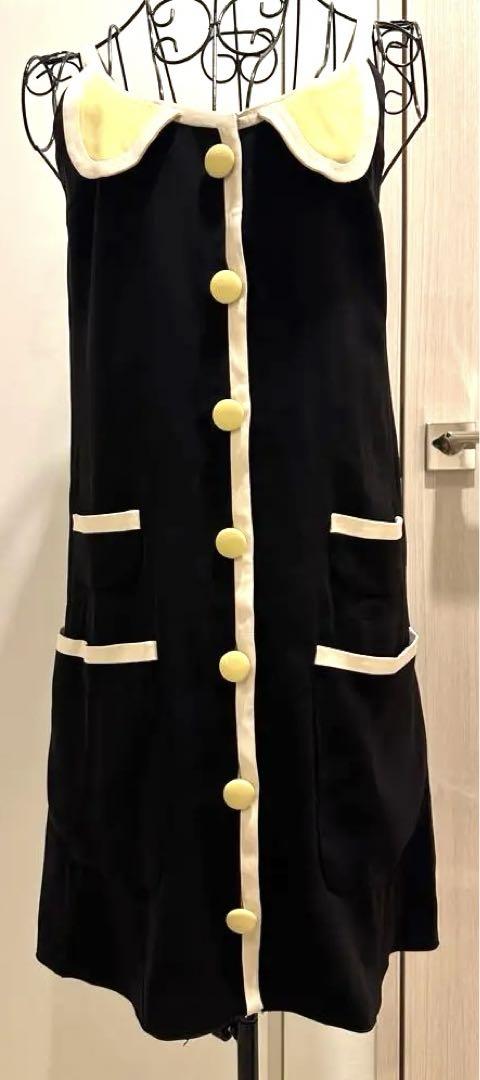 Front view of a black Marc Jacobs silk dress with cream trim, yellow buttons, and pockets displayed on a wire dress form.