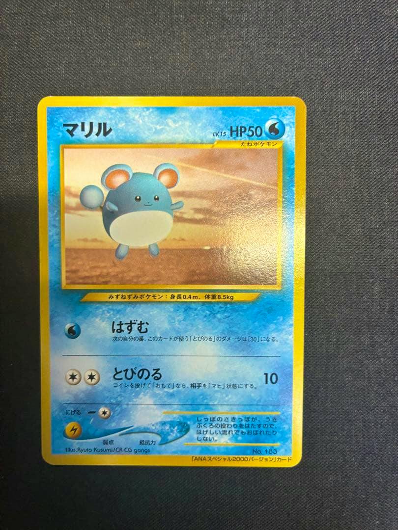Full front of the Japanese Marill trading card (ANA ポケモンジェット "ジェットでゲットだ！2000" promotional) shown on a dark textured background.