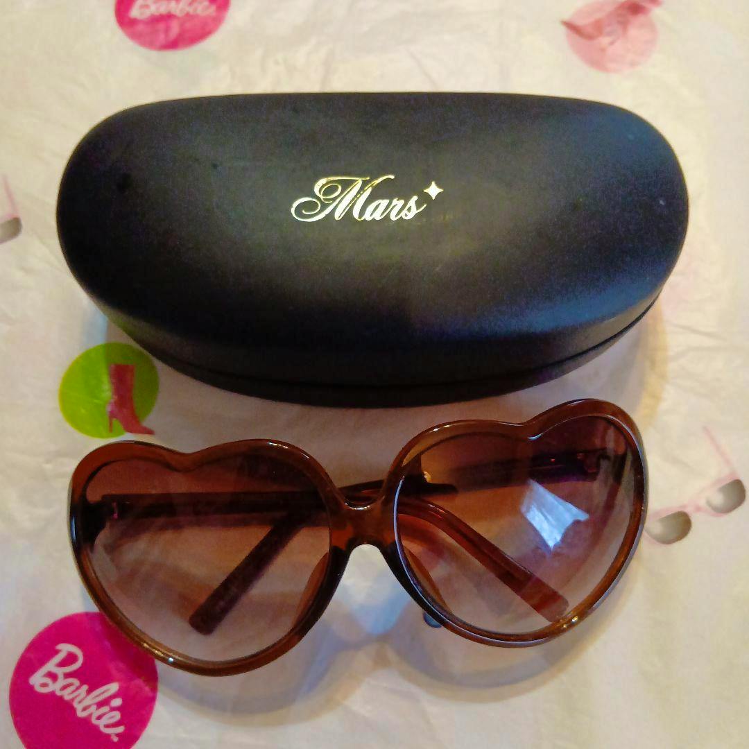 Brown heart-shaped sunglasses with gradient lenses shown in front of a black case stamped "Mars".