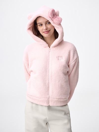 A model wearing a light pink polyester full-zip fluffy hooded women’s jacket with a bow-adorned hood and a small embroidered Sanrio character on the chest.