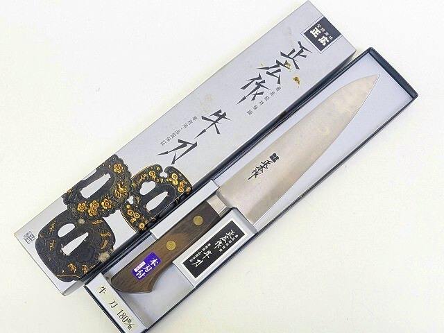 A chef knife laid inside its open box with the decorative outer box beside it.