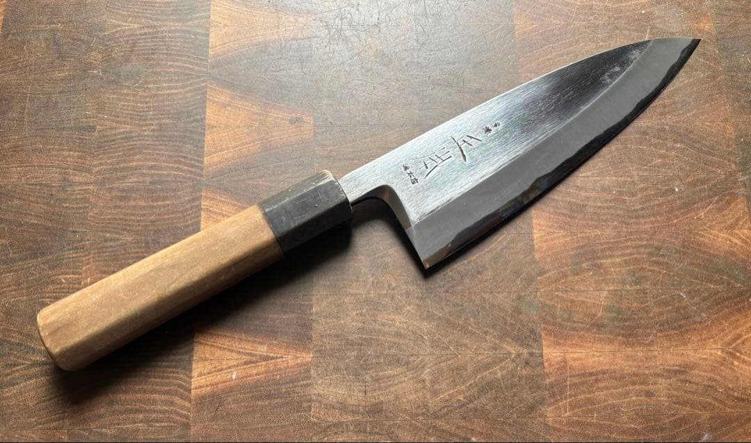 A deba-style Japanese chef knife with a wooden handle and stamped steel blade lying on a wooden cutting board.