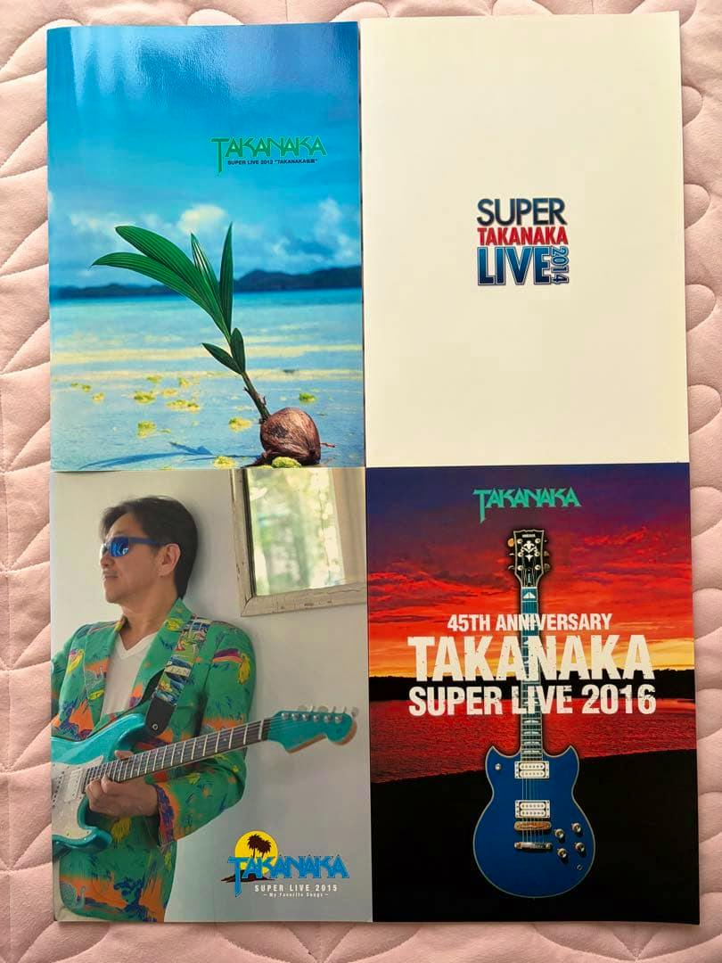 Four tour pamphlets laid out in a 2x2 grid showing various cover art: a beach scene, a white cover with "SUPER TAKANAKA LIVE" text, a portrait of a man with a guitar, and a blue guitar on a sunset background.