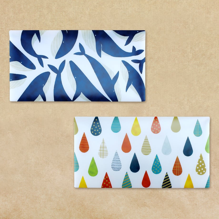 Two rectangular mask cases, one with a blue whale pattern and one with multicolored raindrops, shown on a beige background.