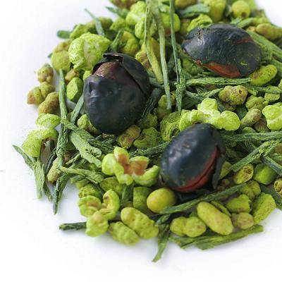 Close-up of a loose green tea blend showing green tea leaves, matcha-coated puffed rice, and black soybeans.