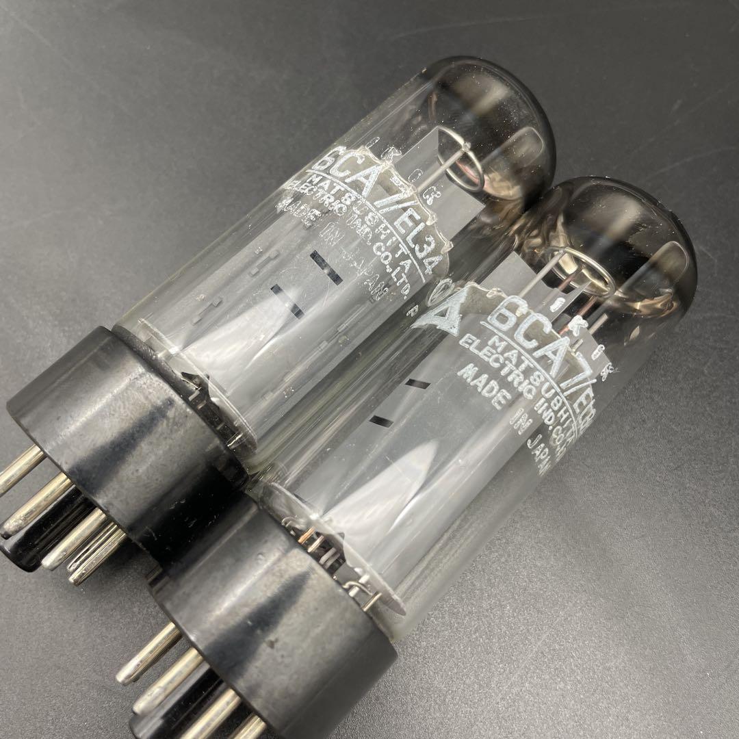 Two 6CA7/EL34 vacuum tubes (one pair) with printed markings, placed side by side on a dark surface.