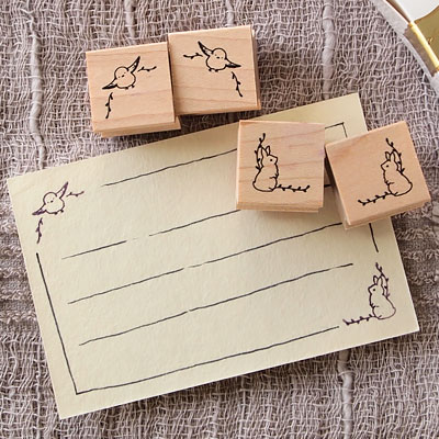 Four small wooden rubber stamps with corner animal designs arranged on fabric beside a paper card showing their stamped corner decorations.