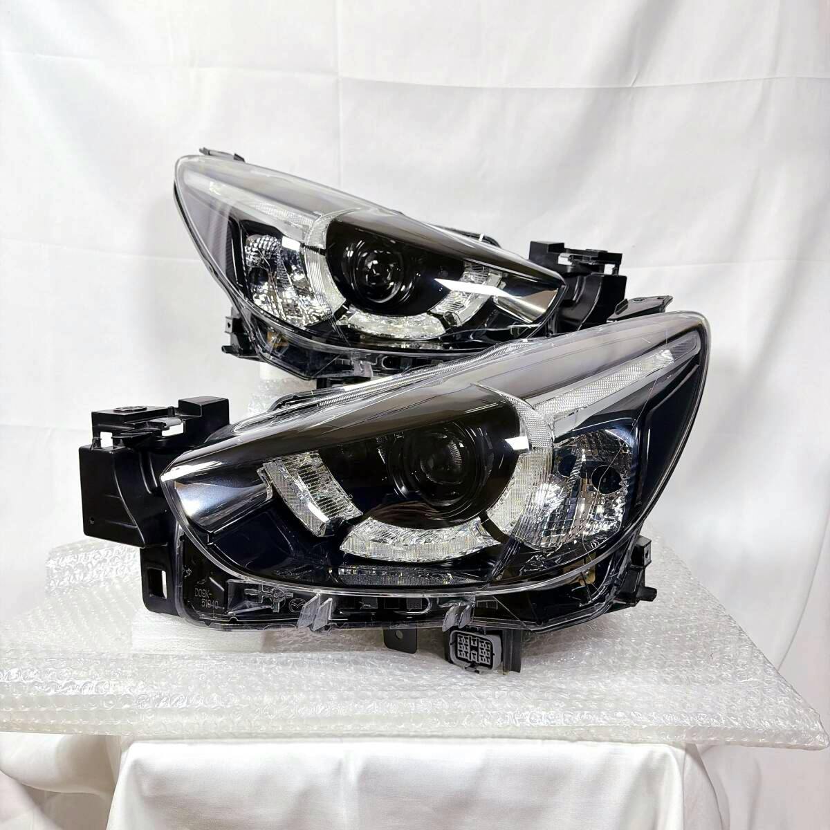 Two Mazda Demio DJ-series headlight assemblies (left and right) displayed on bubble wrap against a white backdrop.