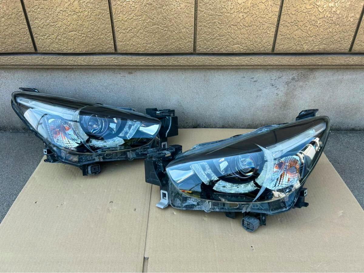 Front view of two Mazda Demio (DJ5FS) headlight assemblies placed on cardboard, lenses visible.