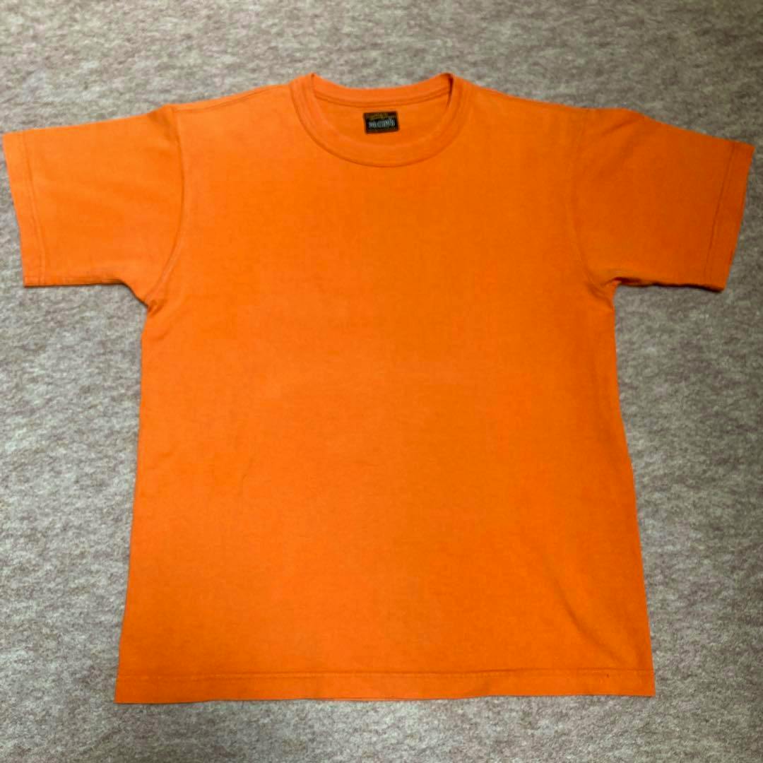 Front view of an orange McCOY'S Tシャツ laid flat on a gray surface.