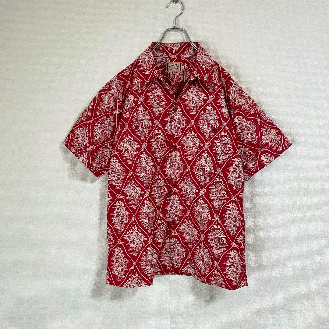 Red McCoy Sportswear rayon men's aloha (Hawaiian) shirt with a white cowboy pattern hanging on a hanger against a wall.