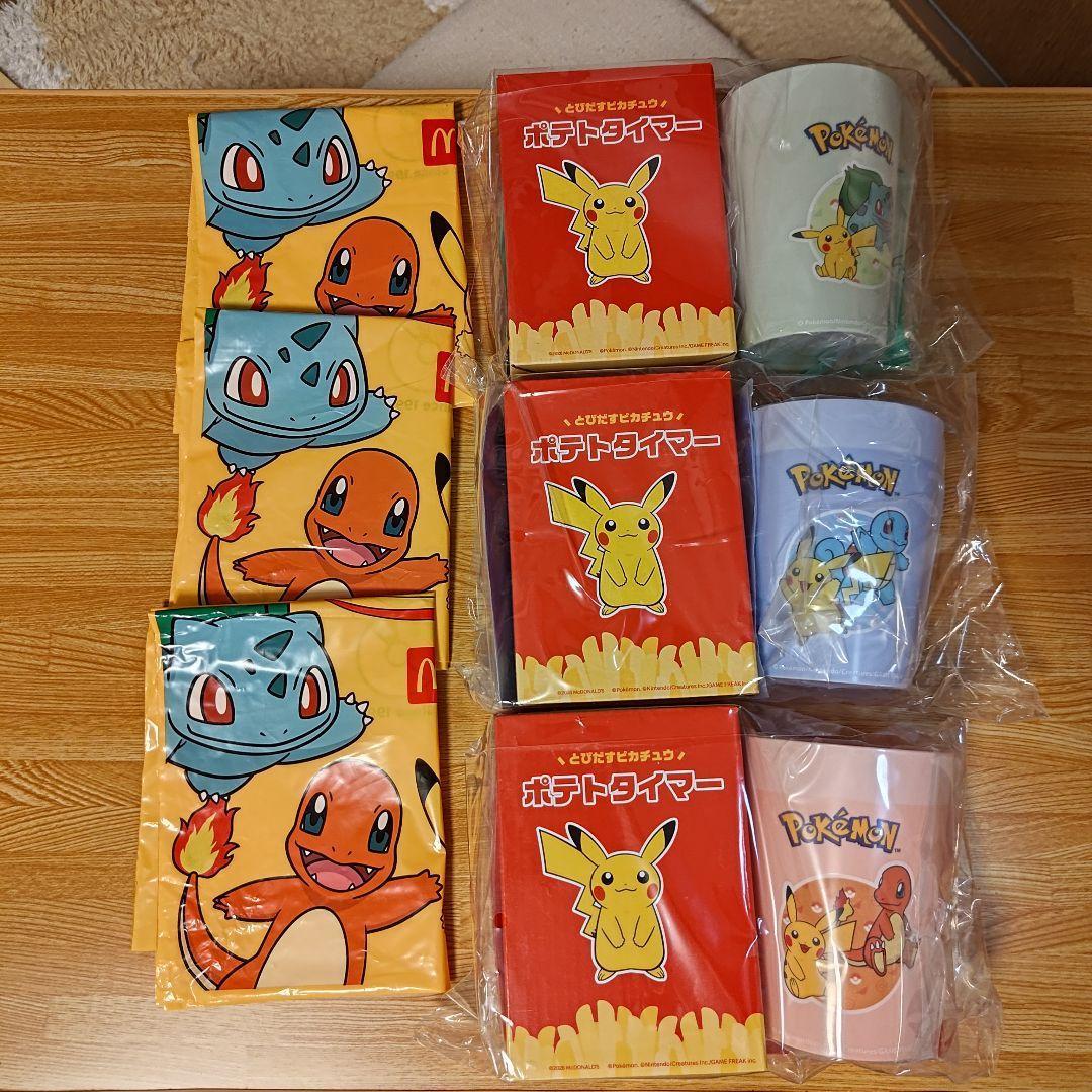 Packaged plastic Pokémon cups and matching McDonald’s 2026 summer goods displayed with three red Pikachu boxes and folded Pokémon-printed bags on a wooden surface.
