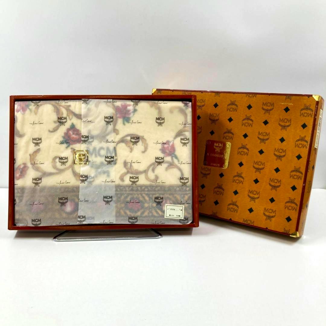 MCM bath towel in a gift box wrapped with branded tissue paper, shown next to its MCM-patterned outer box.