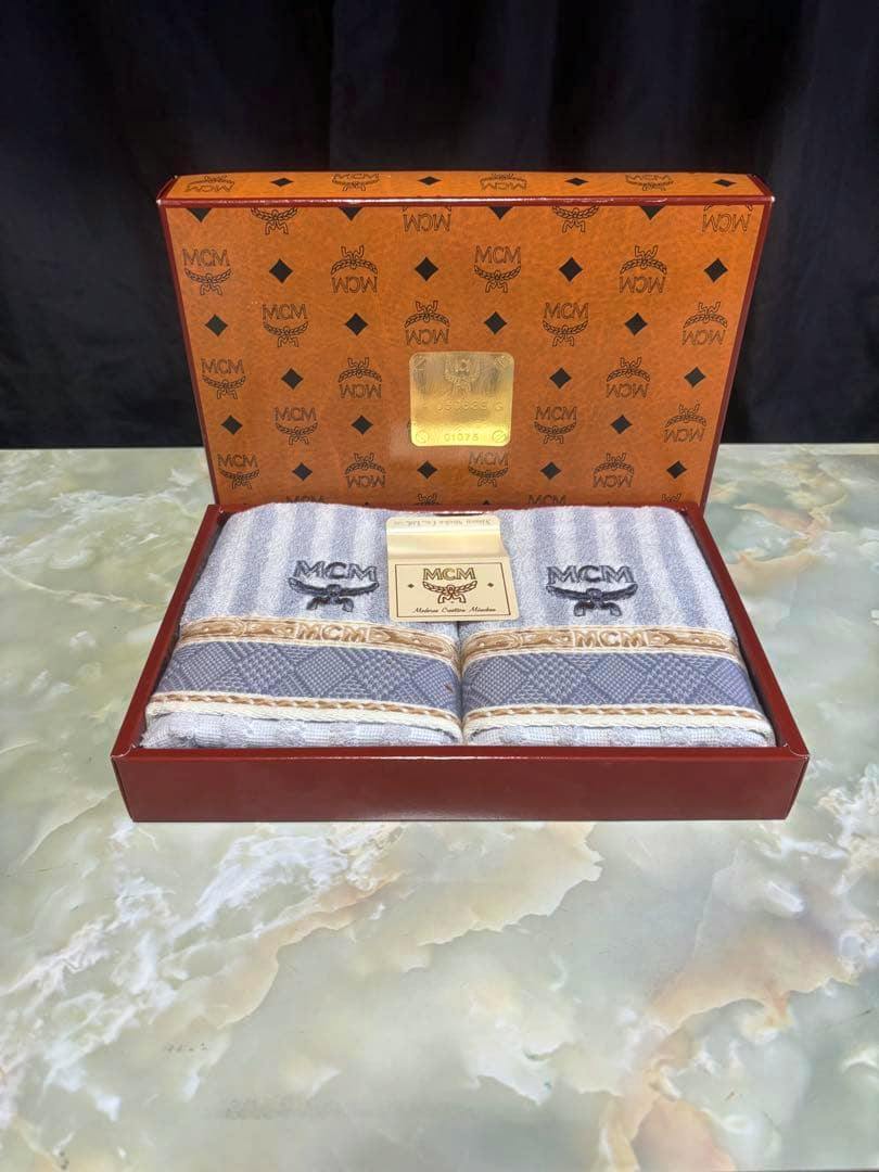 Open MCM gift box with two folded face towels displayed inside.