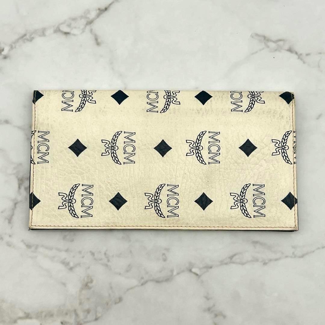 White MCM long wallet with repeating black MCM logos and diamond motifs shown flat on a marble surface.