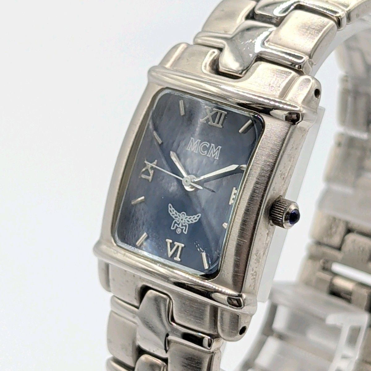 Silver square MCM men's quartz wristwatch with metal bracelet and the MCM logo visible on the dial.