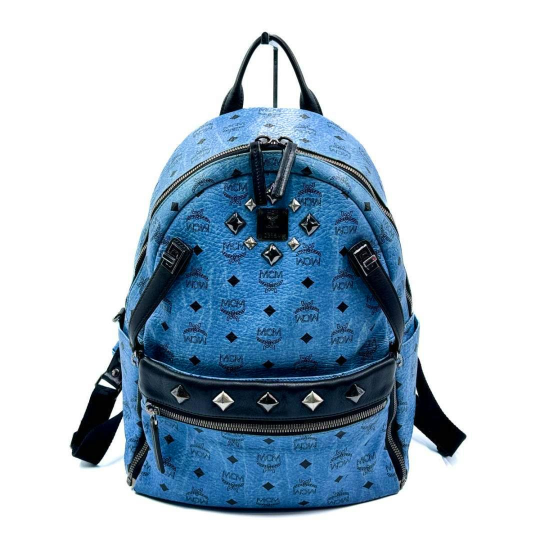 Front view of a blue MCM Visetos canvas backpack with studs, black accents, and a front zip pocket.