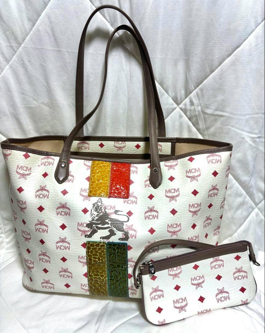 White MCM Visetos tote shoulder bag with brown handles, multicolored textured vertical stripes and a matching pouch.