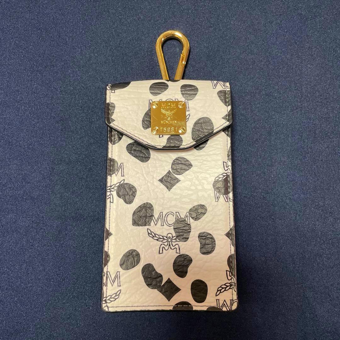 Front view of the MCM × LOVELESS leopard-print small leather case showing the gold MCM plaque and top clasp.